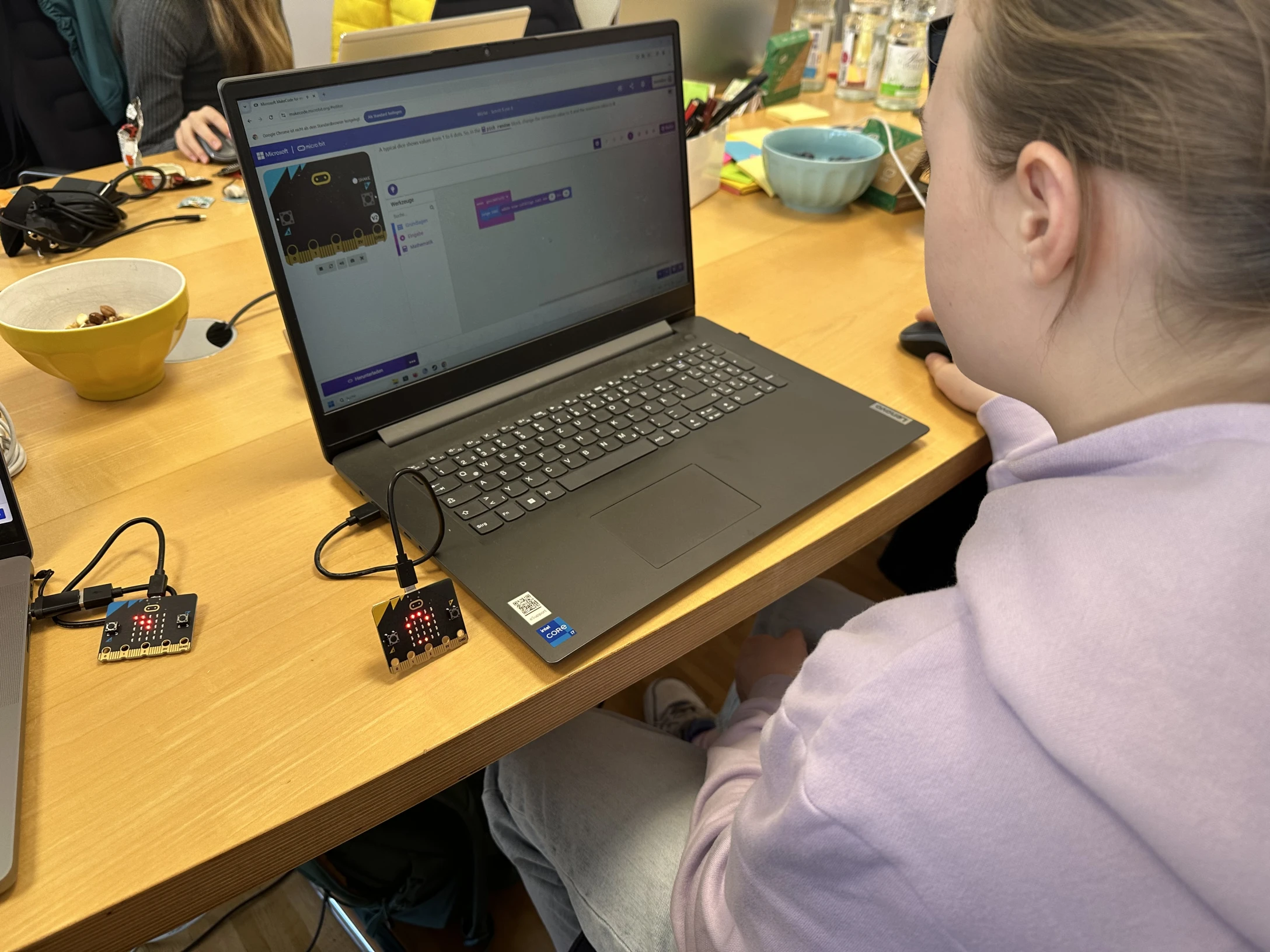 Mädchen setzt an einem Notebook die nötigen Programmierbausteien zusammen. Danaben liegt der microbit Controller auf dem Tisch