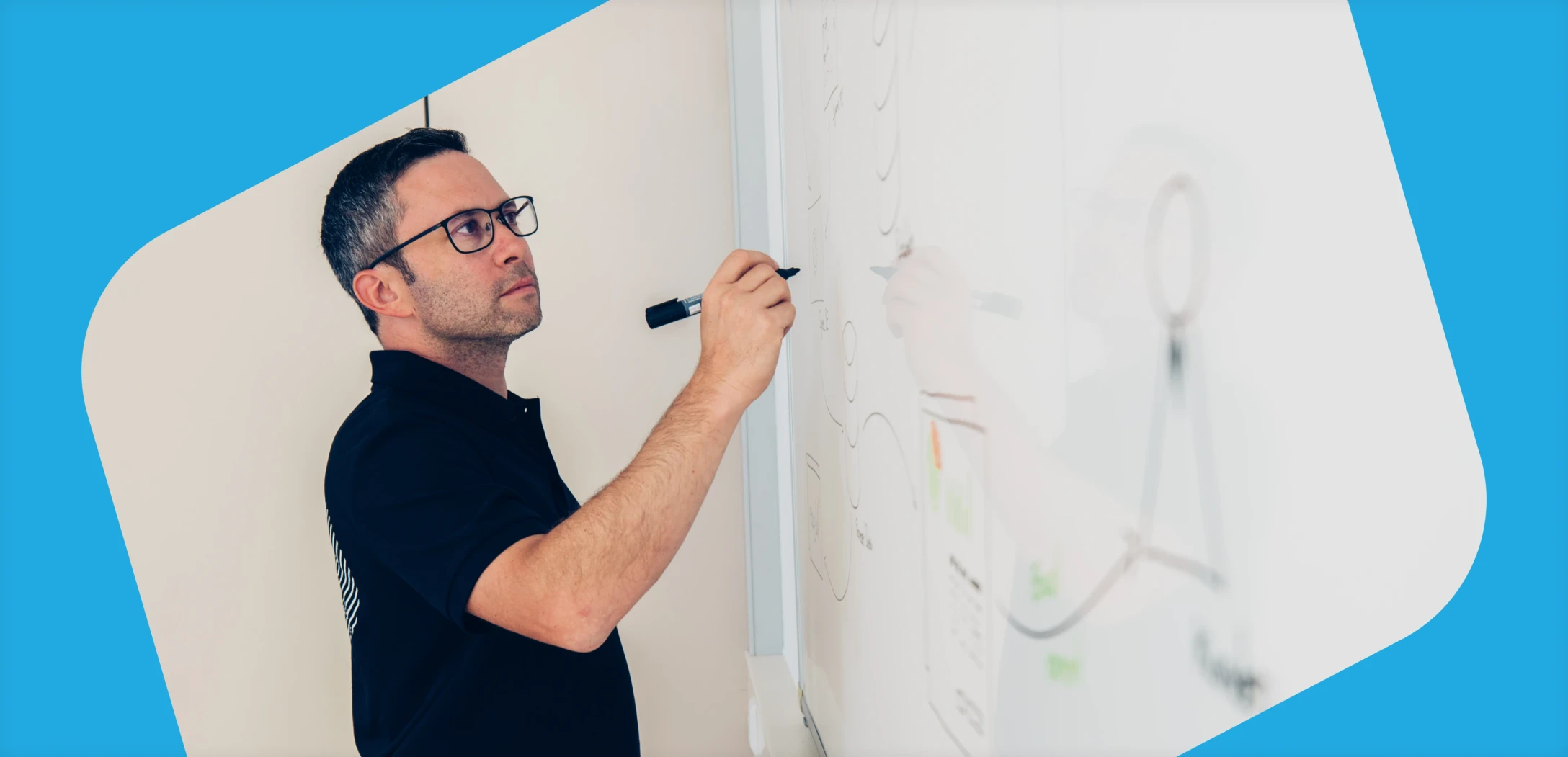 Ein Mann mit Brille zeichnet auf einem Whiteboard.
