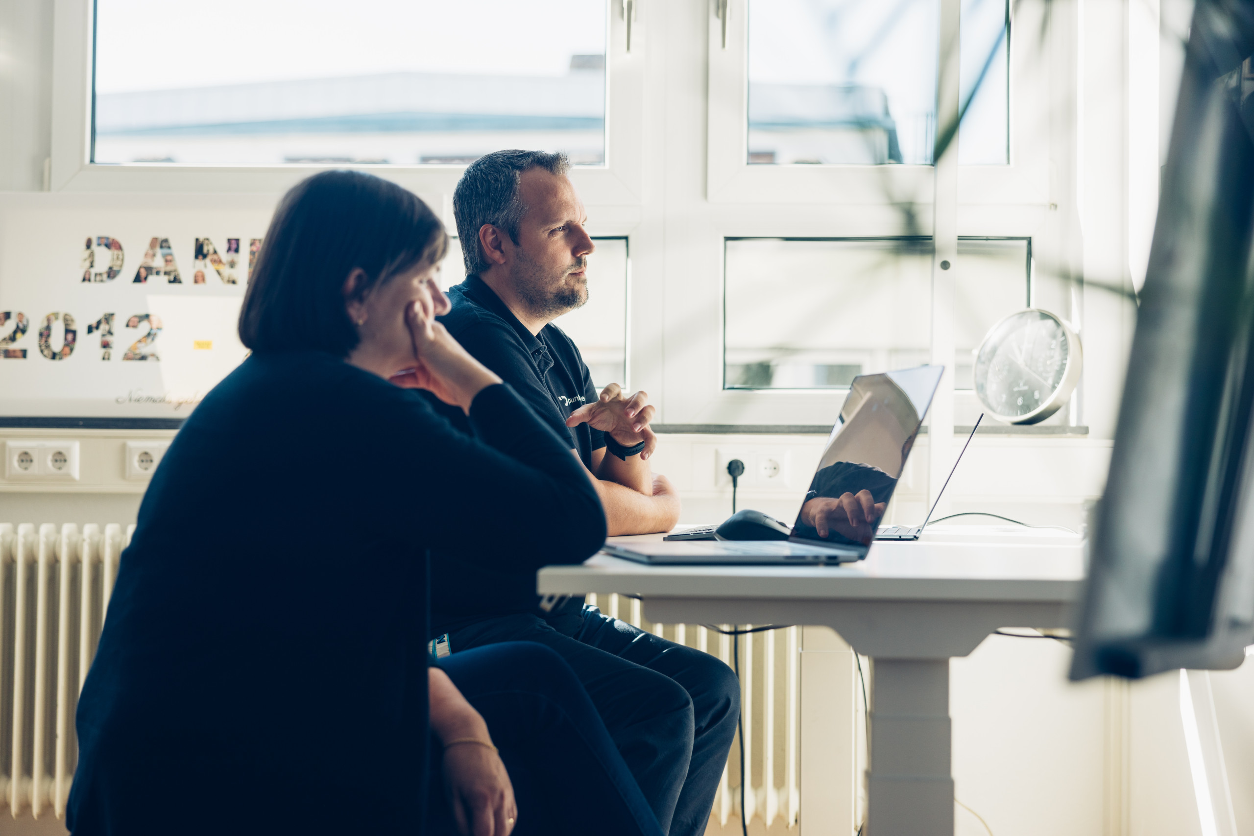 Ein Mann und eine Frau sitzen im Büro an einem Schreibtisch und besprechen etwas